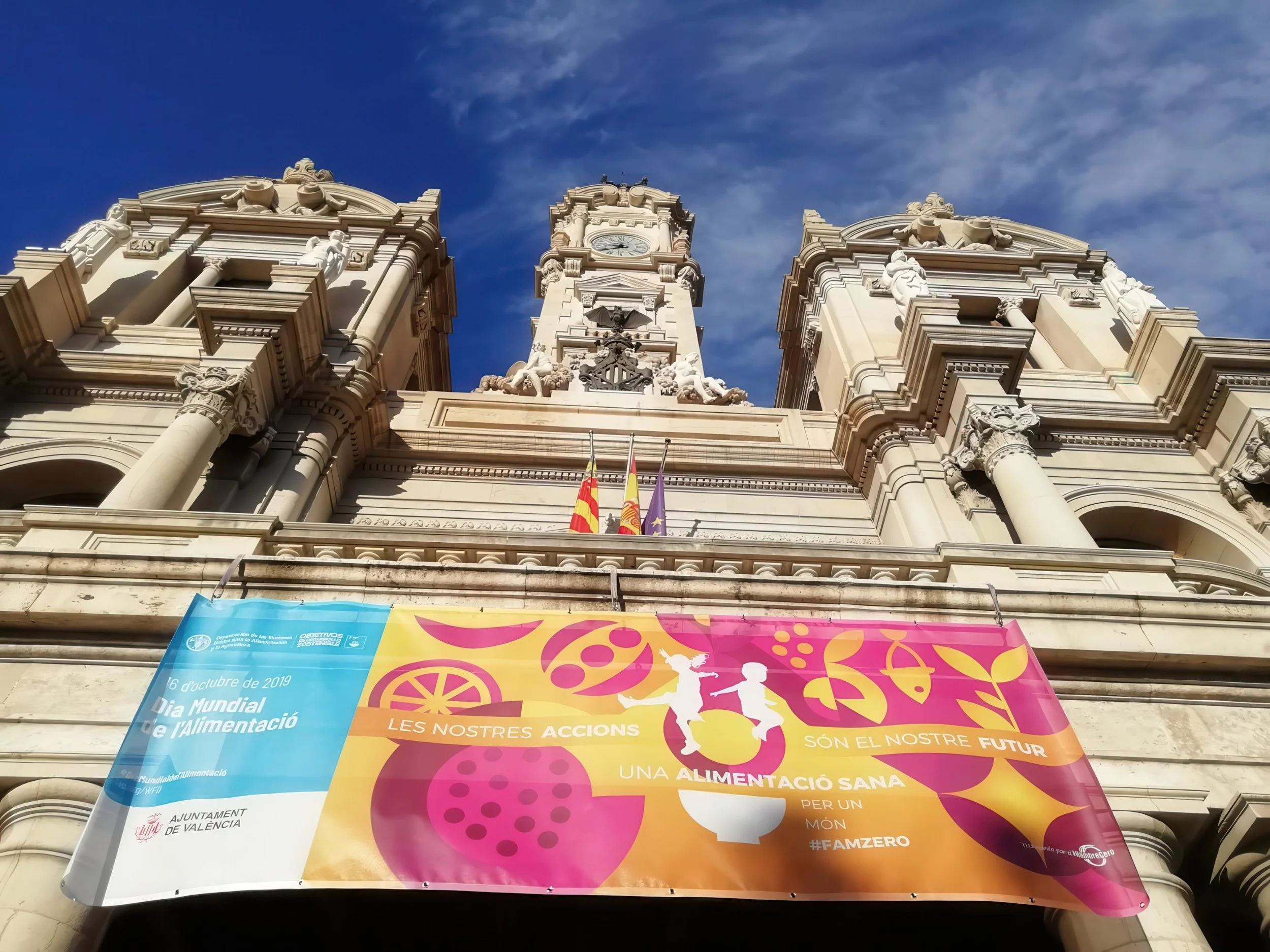 Photo of a historic building with ornate architecture and a clock tower against a blue sky. Colorful banners related to World Food Day are hanging in front of the building.
