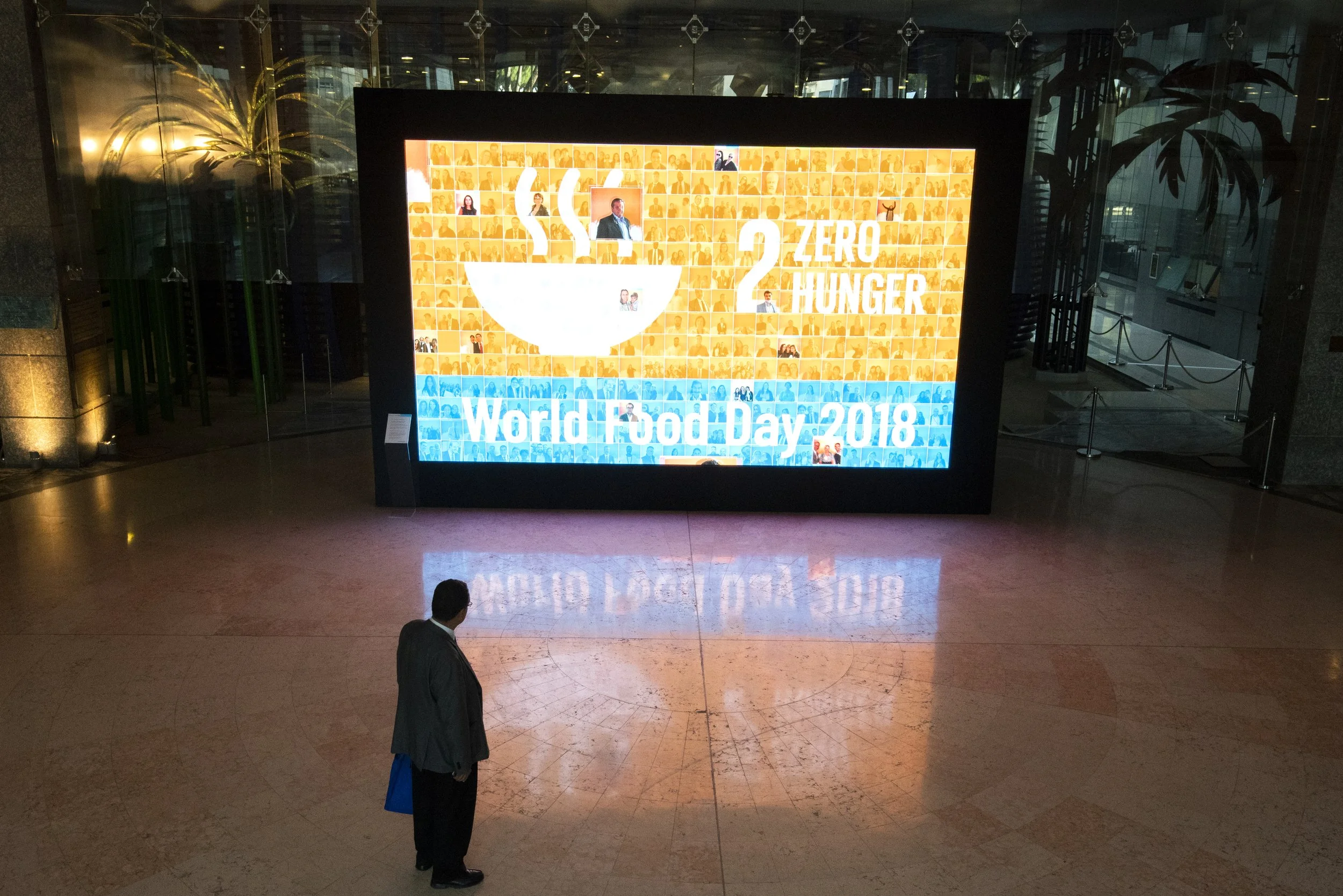 A digital display board showing information about World Food Day 2018, highlighting the goal of zero hunger, with a large bowl icon and numerous small images of people.