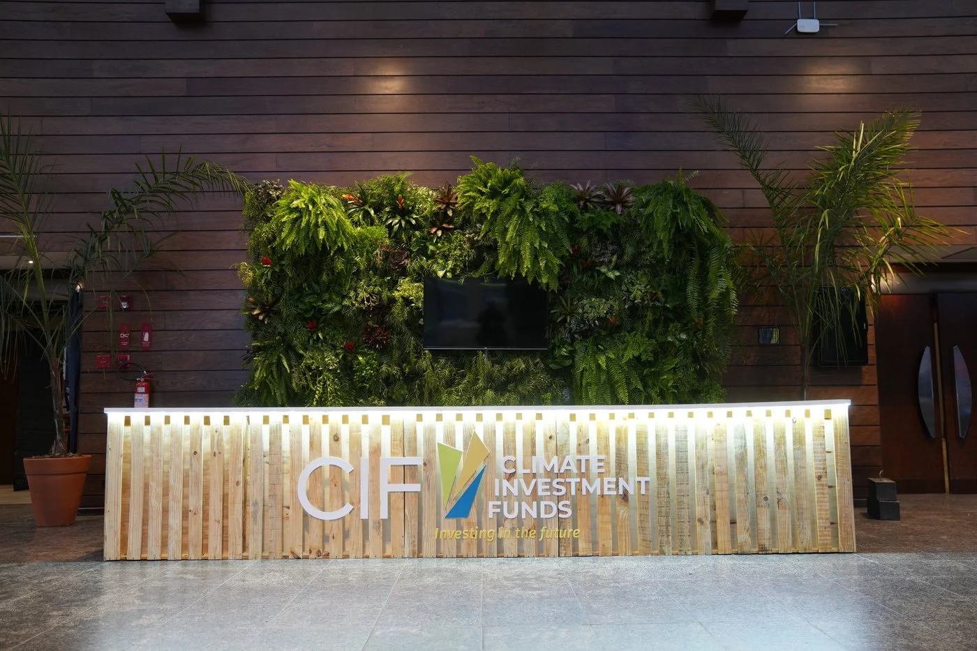 Reception desk with a sign for Climate Investment Funds, decorated with green plants and a wooden backdrop.