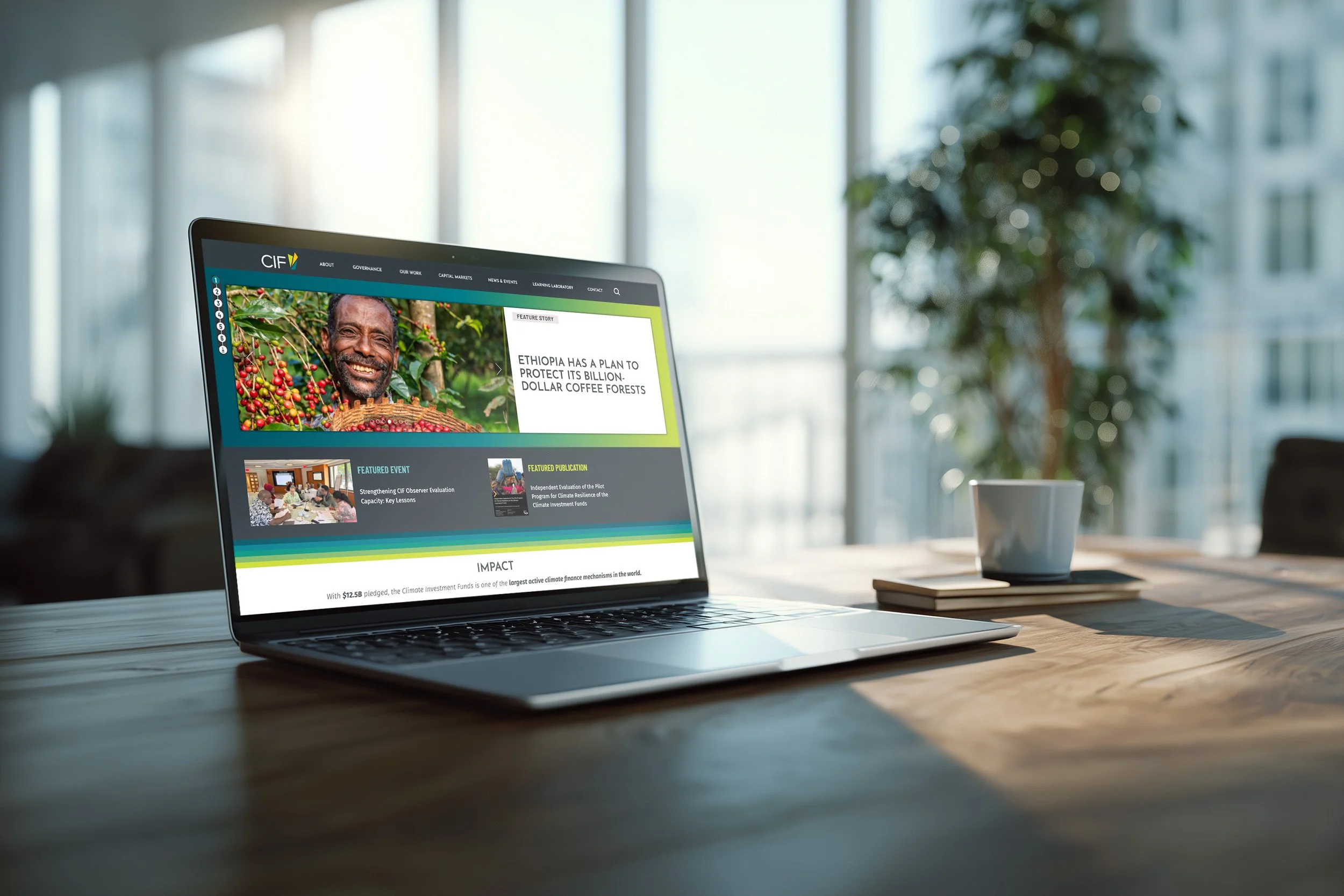 A laptop on a wooden table displaying a website about Ethiopian coffee, with a smiling man holding coffee beans in a coffee plantation, in a bright room with large windows and a potted plant in the background.