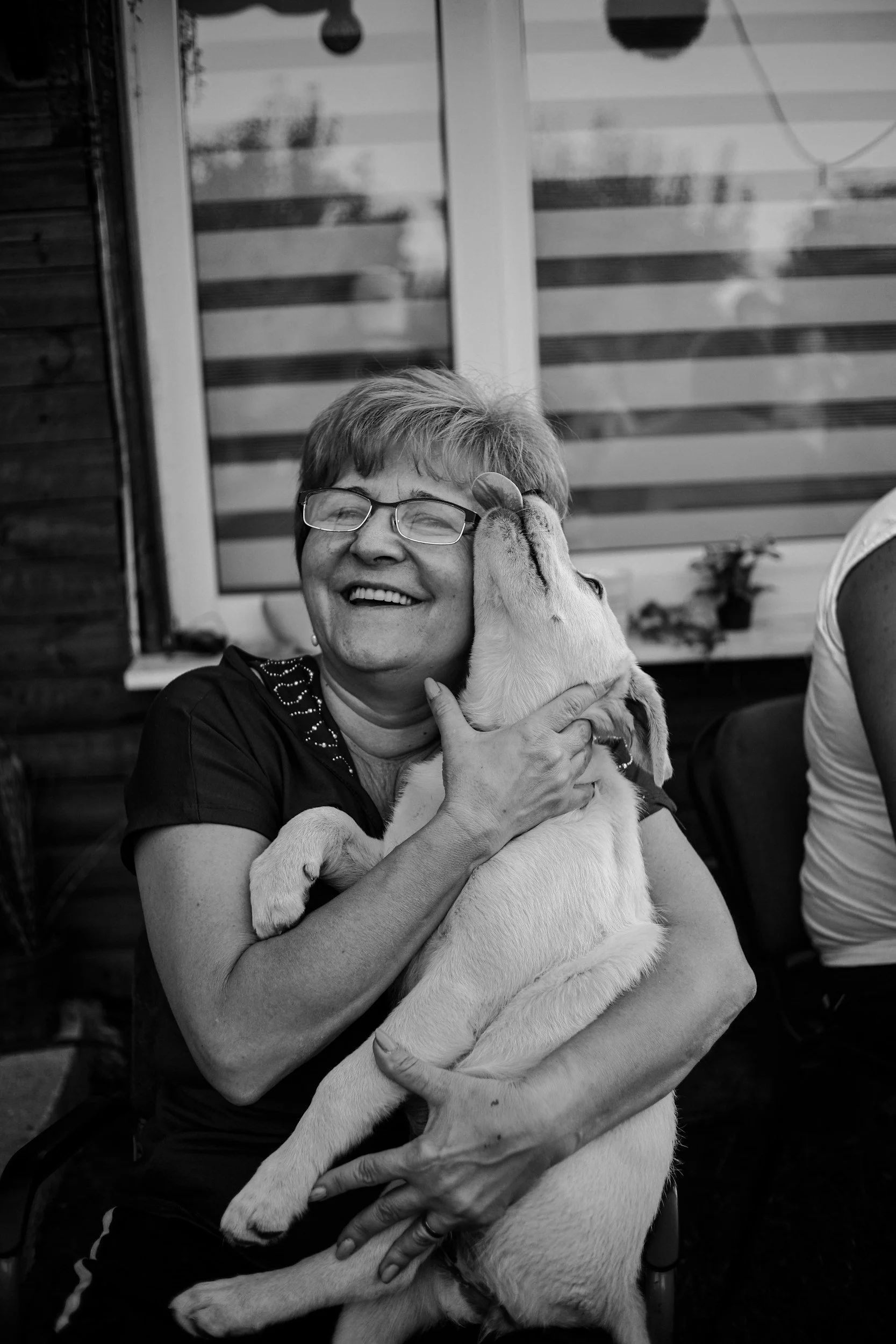 A woman with glasses smiling while hugging a young puppy.
