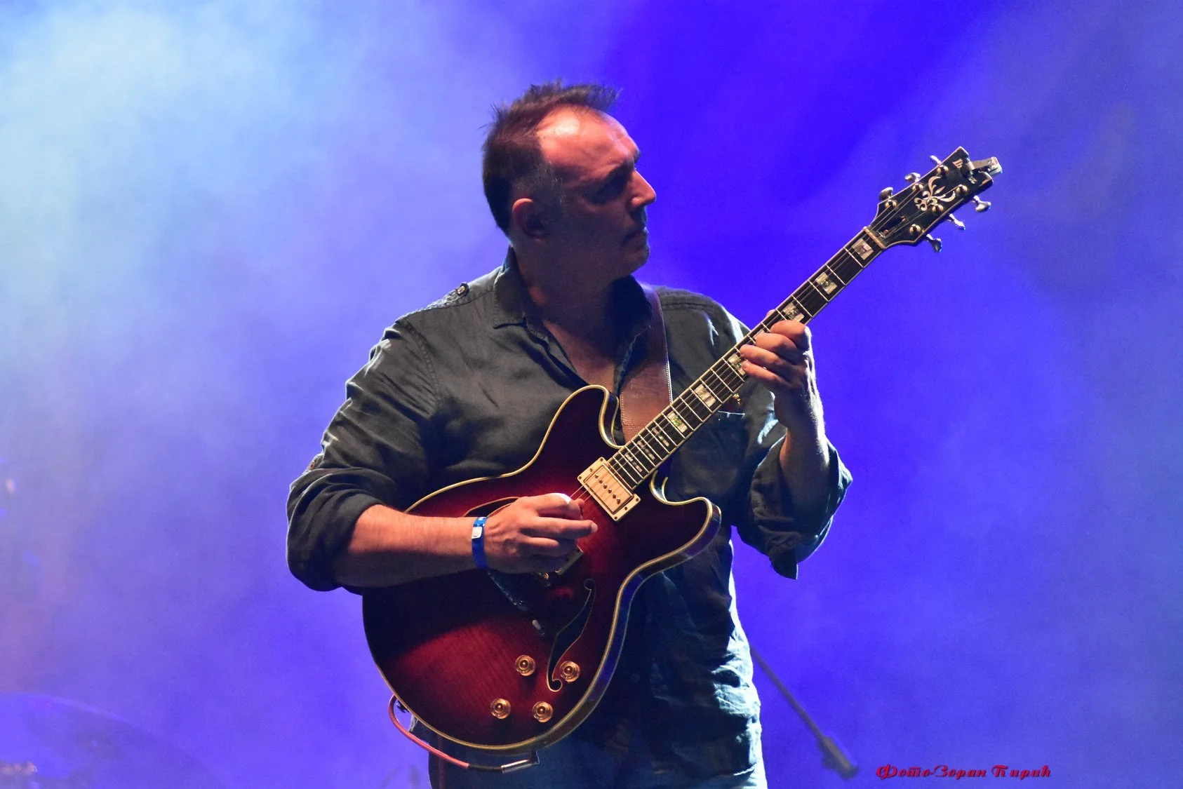 A man playing an electric guitar on stage with blue and purple lighting.