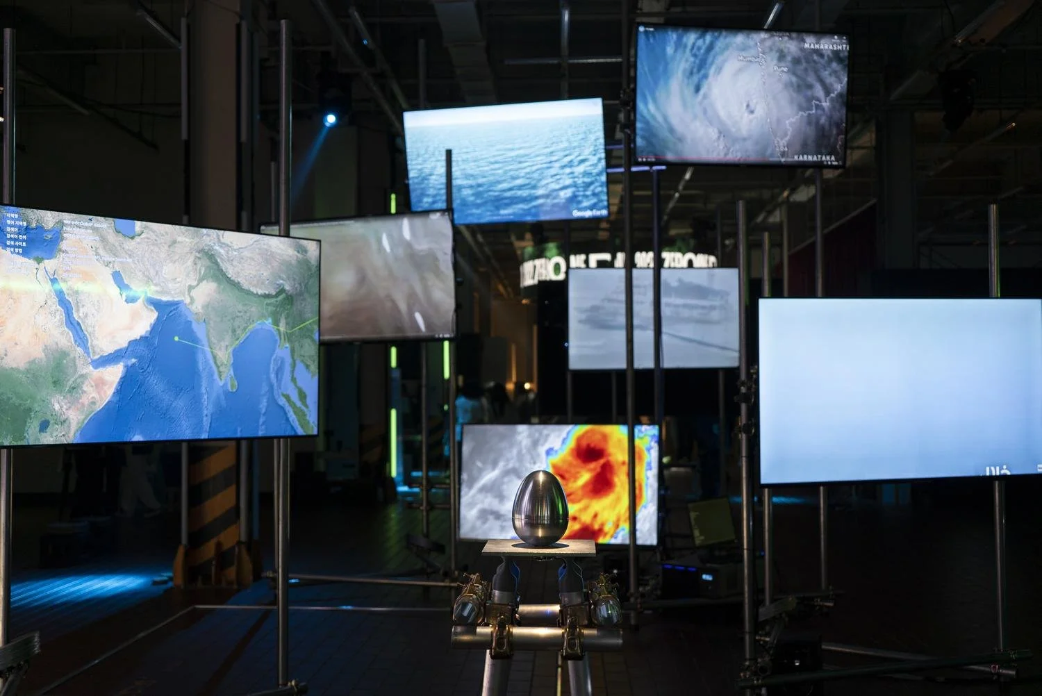 Multiple screens displaying weather, satellite images, and maps in a dark room, with a metal robot in the foreground.