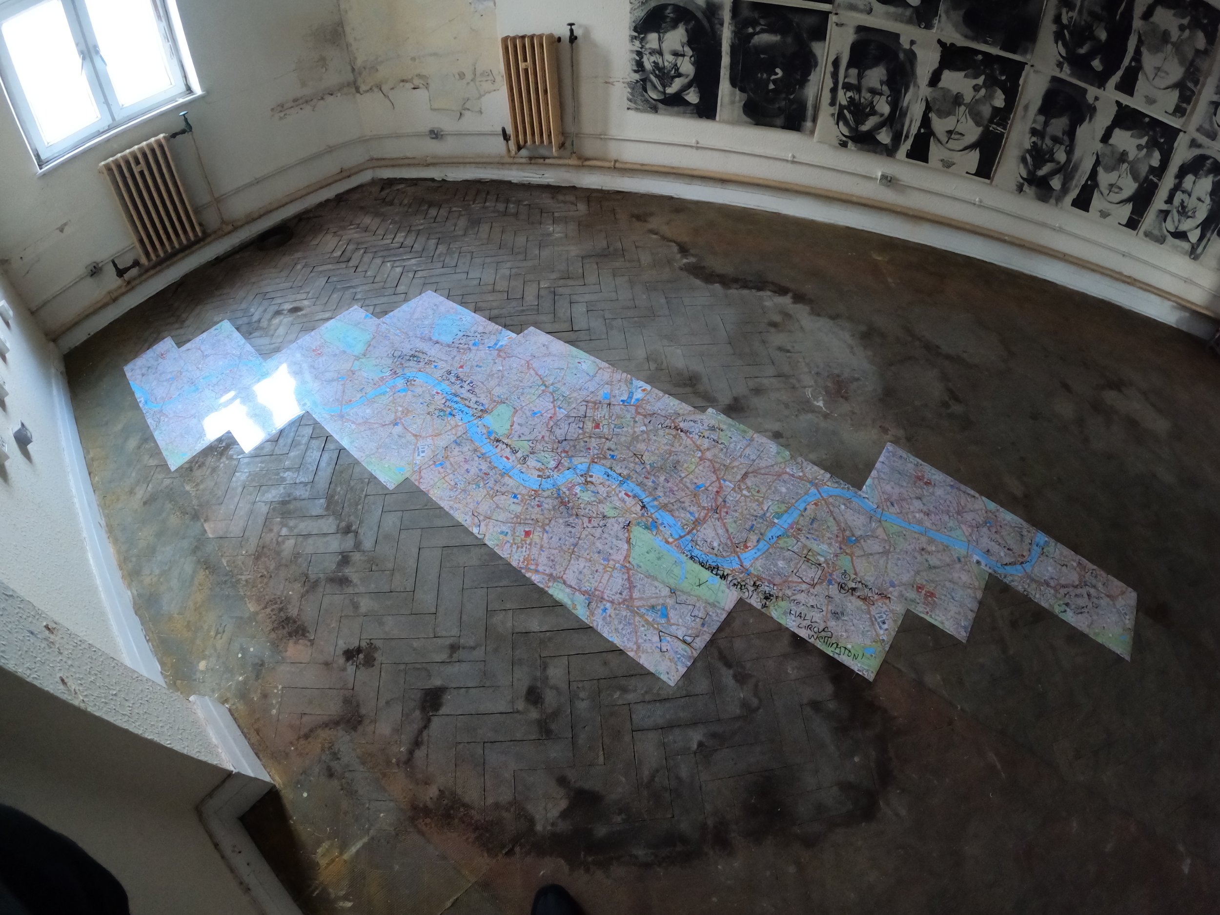 An empty room with a window, radiator pipes, and wall art, featuring a map laid out on the floor.