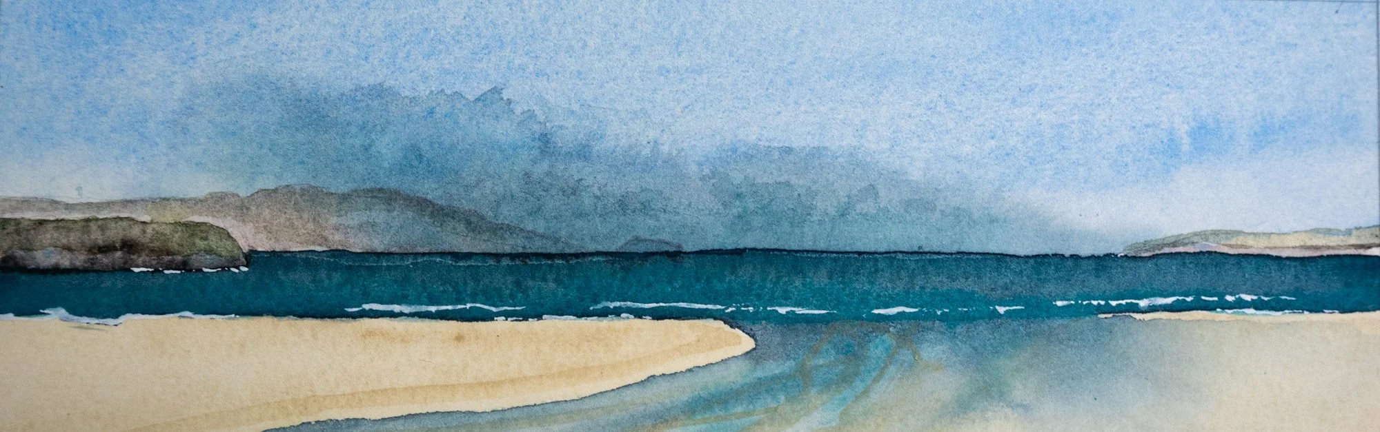 Waves breaking on a sunlit beach. Headland in the middle distance is in sun. A distant headland is enveloped in low fog