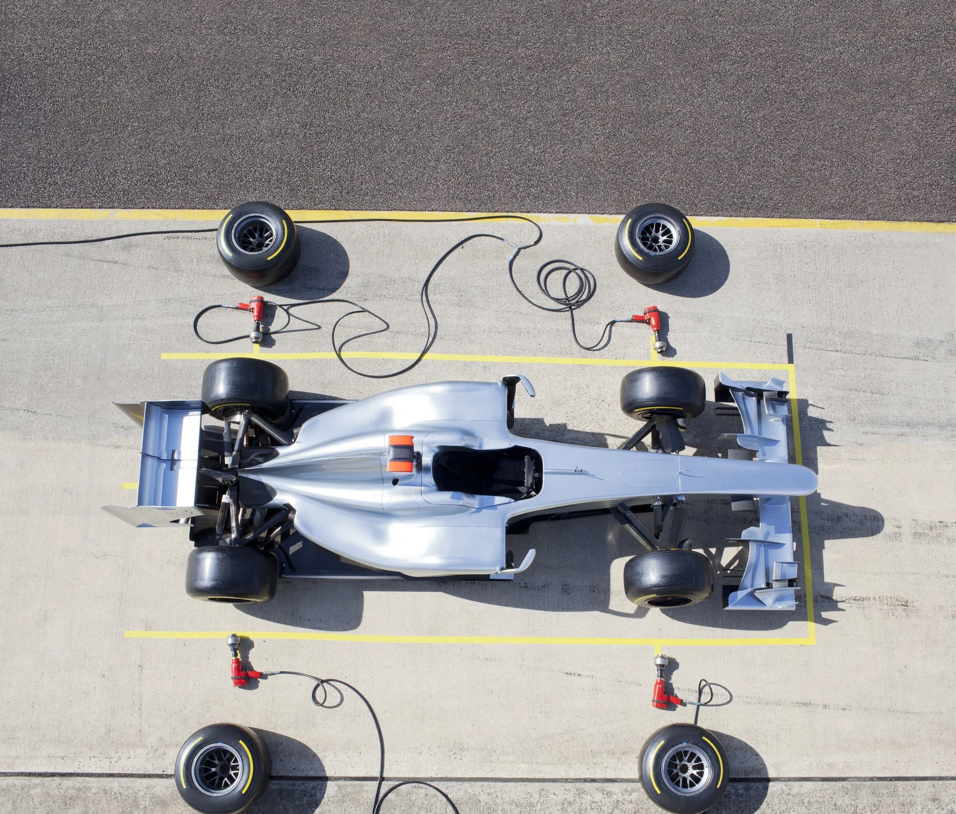 An aerial view of a racing car on a pit stop area connected to tire warmers and air hoses.