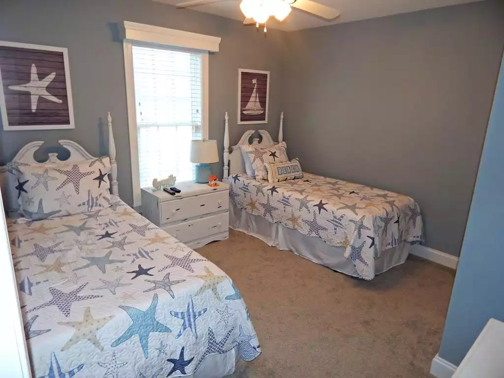 A bedroom with two twin beds decorated with starfish-themed bedding, a white nightstand with a lamp, and nautical-themed wall art of a starfish and a sailboat.