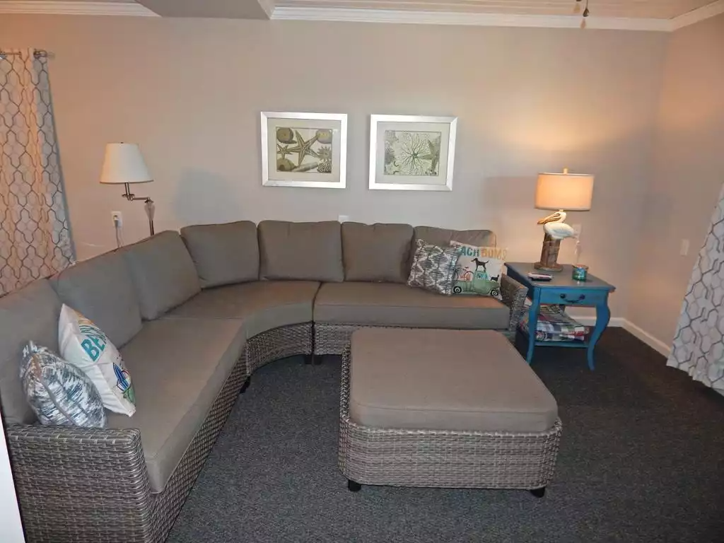 Living room with a sectional sofa, a matching ottoman, a side table with a lamp, decorative pillows, and framed artwork on the wall.