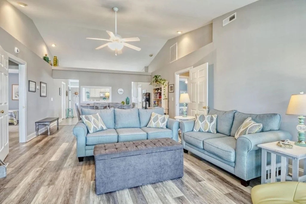Living room with two light blue sofas, patterned pillows, a vaulted ceiling with a ceiling fan, lamps, and wood flooring.