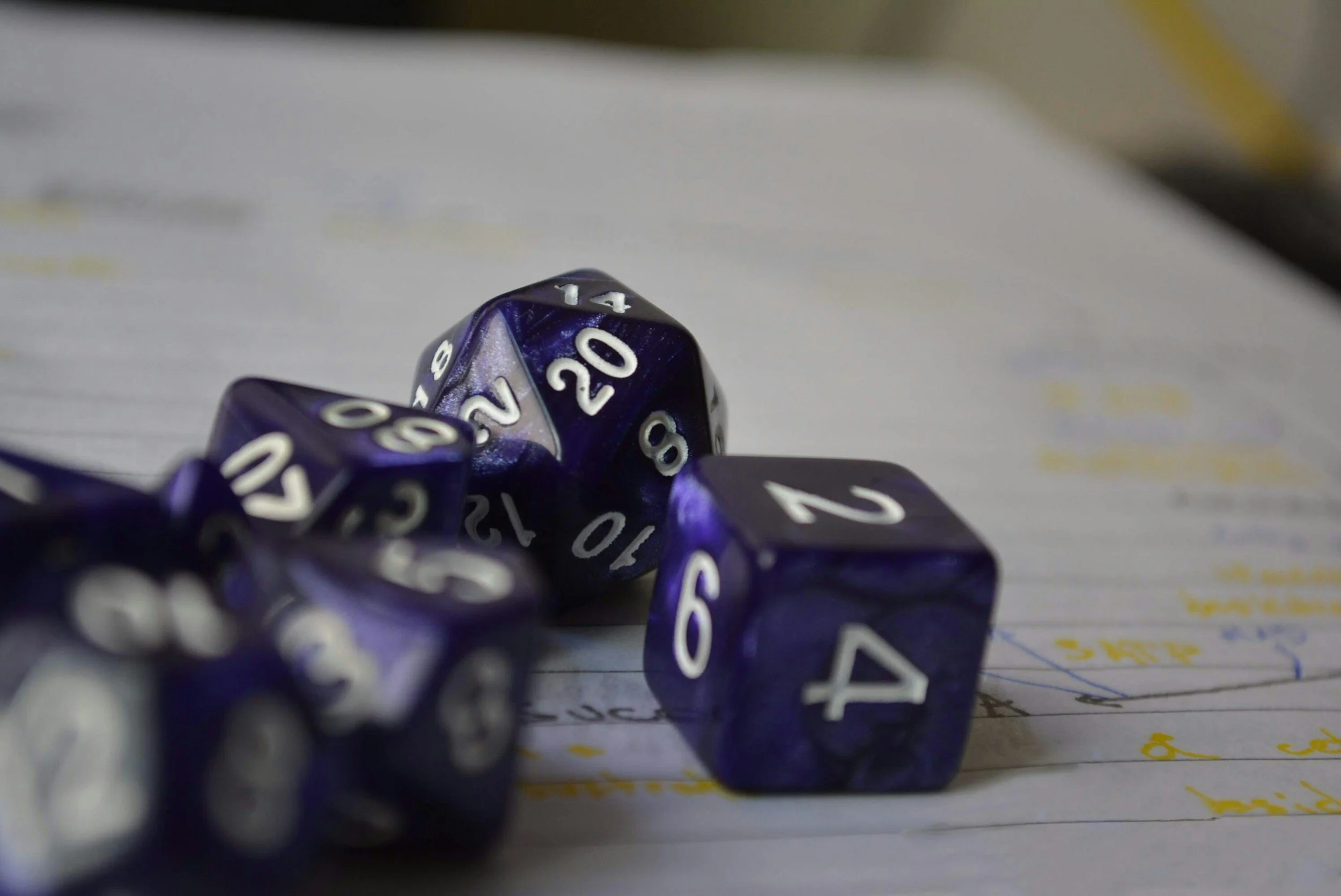A pile of multi-sided purple and black twenty-sided dice with white numbering resting on a piece of paper with handwritten notes.