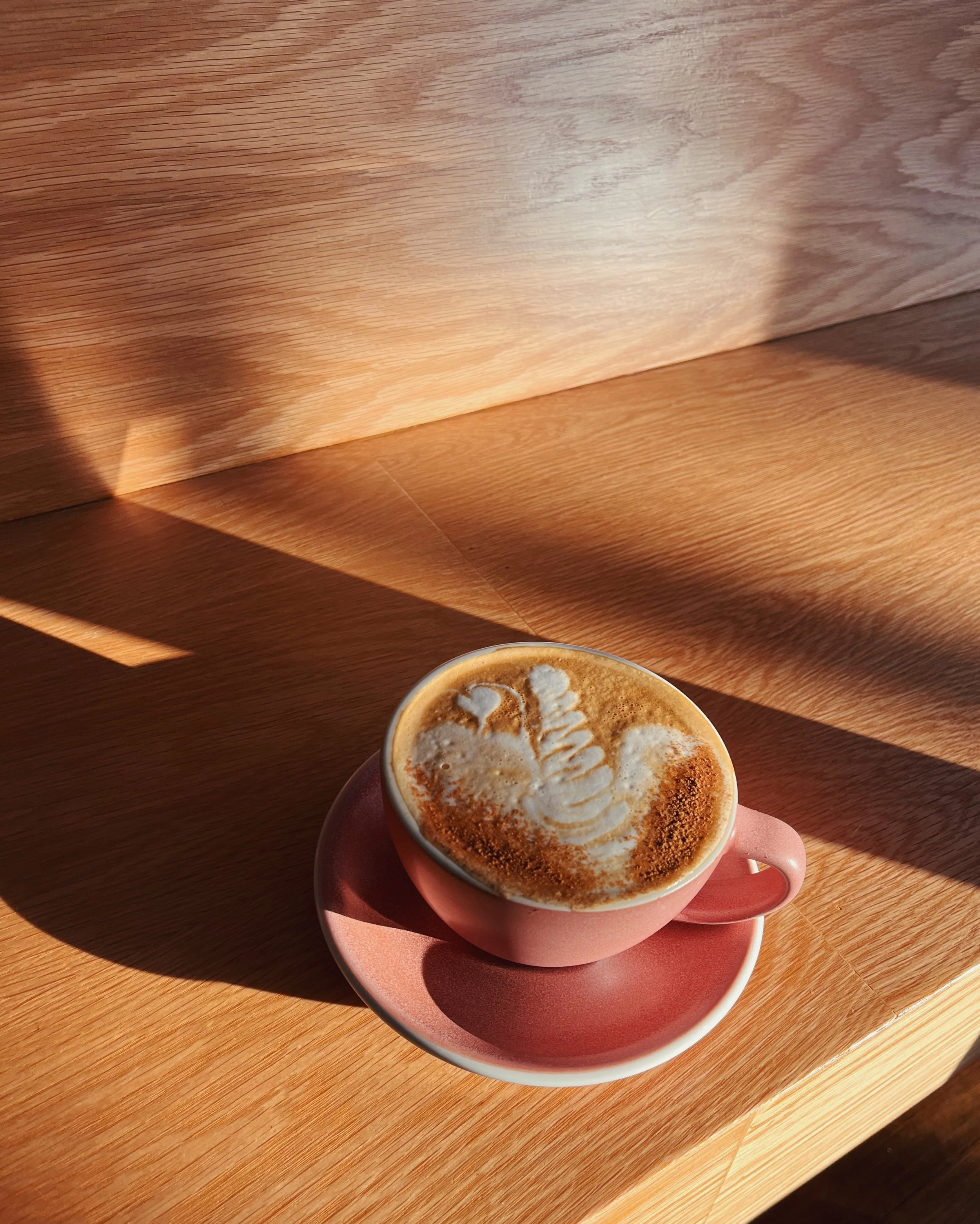A cup of latte coffee with foam art on top, placed on a pink saucer on a wooden table.