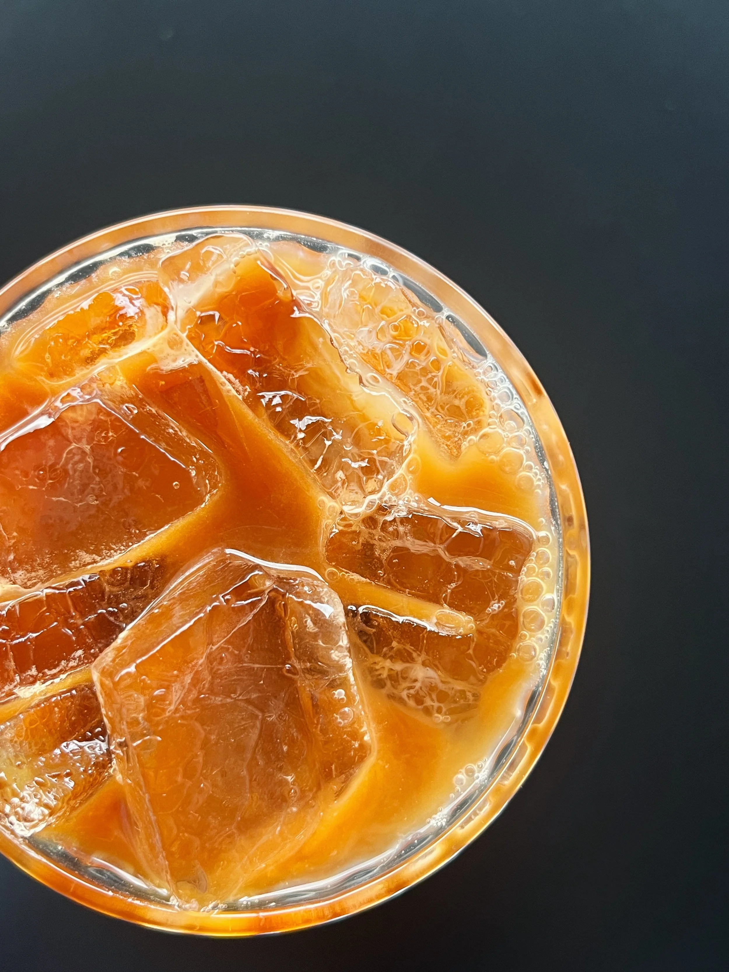 A glass of iced orange-colored beverage with ice cubes, placed on a dark surface.
