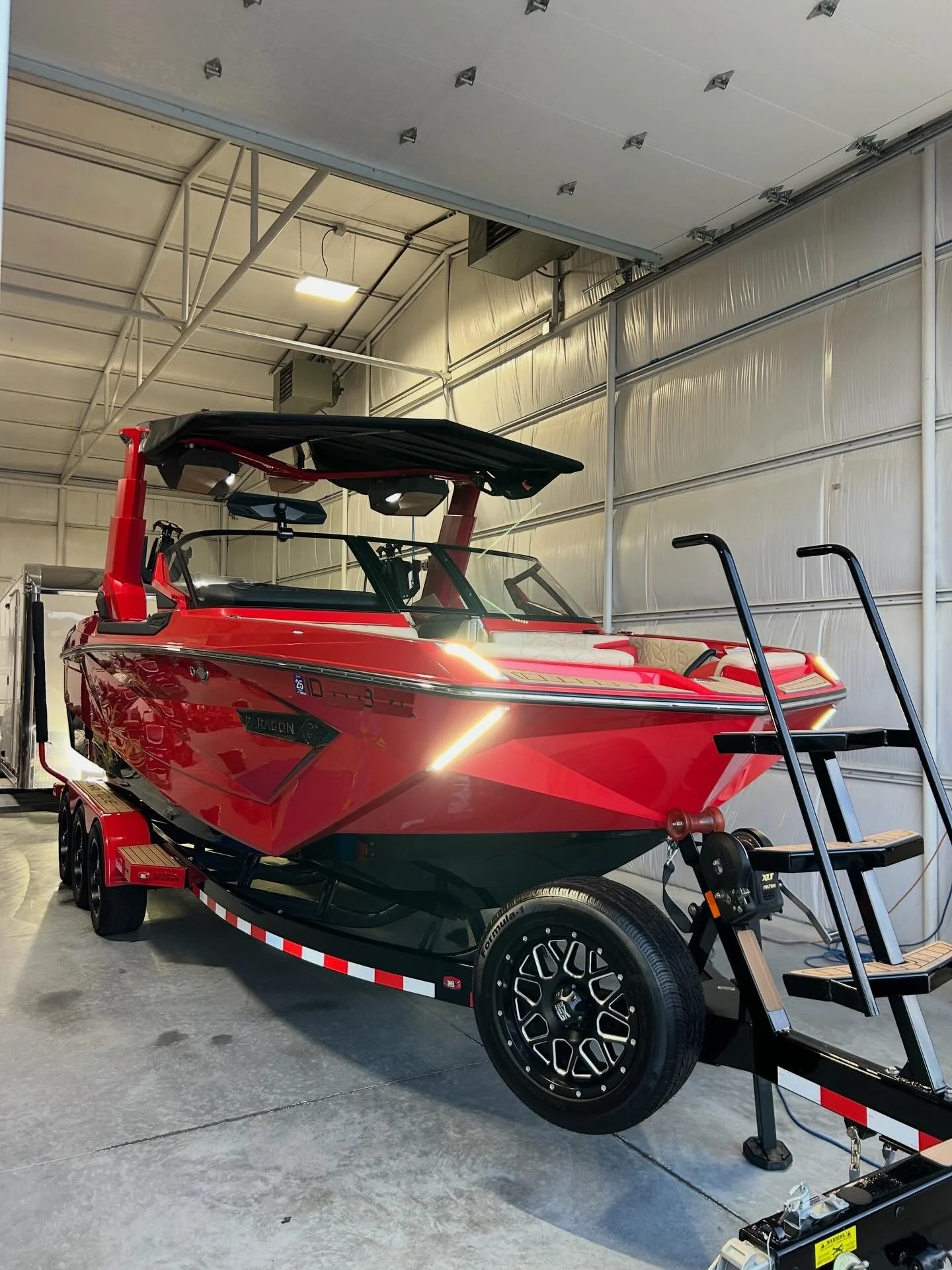 A red and black Nautique boat on a trailer inside a large garage or warehouse with metal walls and ceiling.