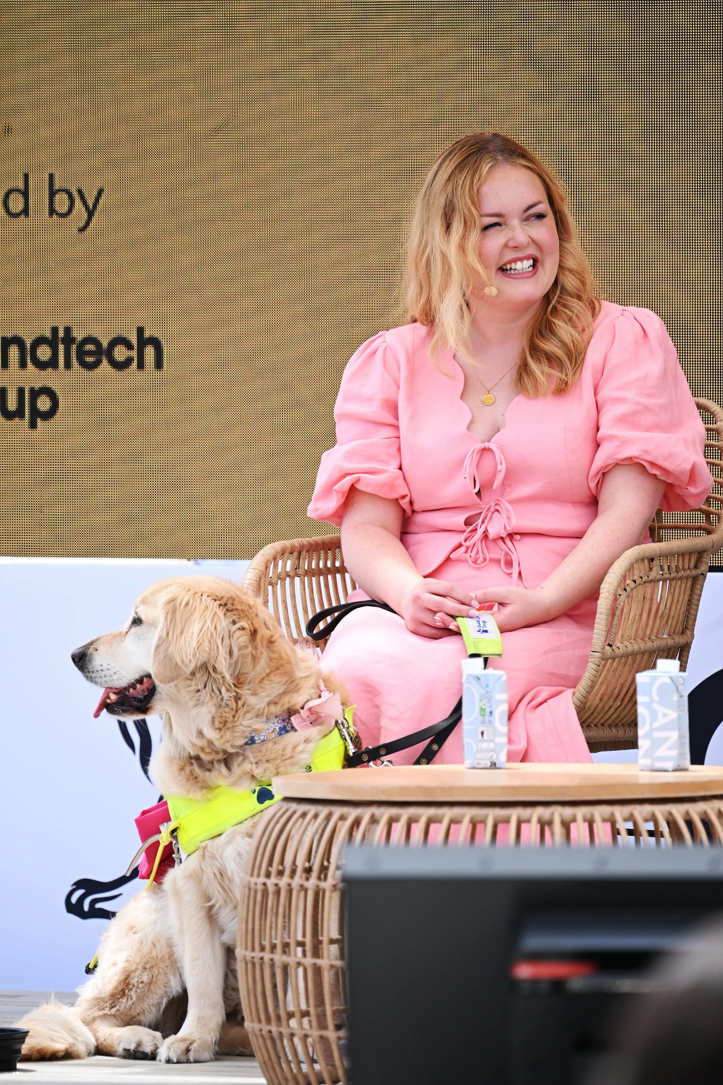 Lucy wears a pink co-ord and sits on a wicker chair next to golden retriever Molly on the stage at Cannes Lions