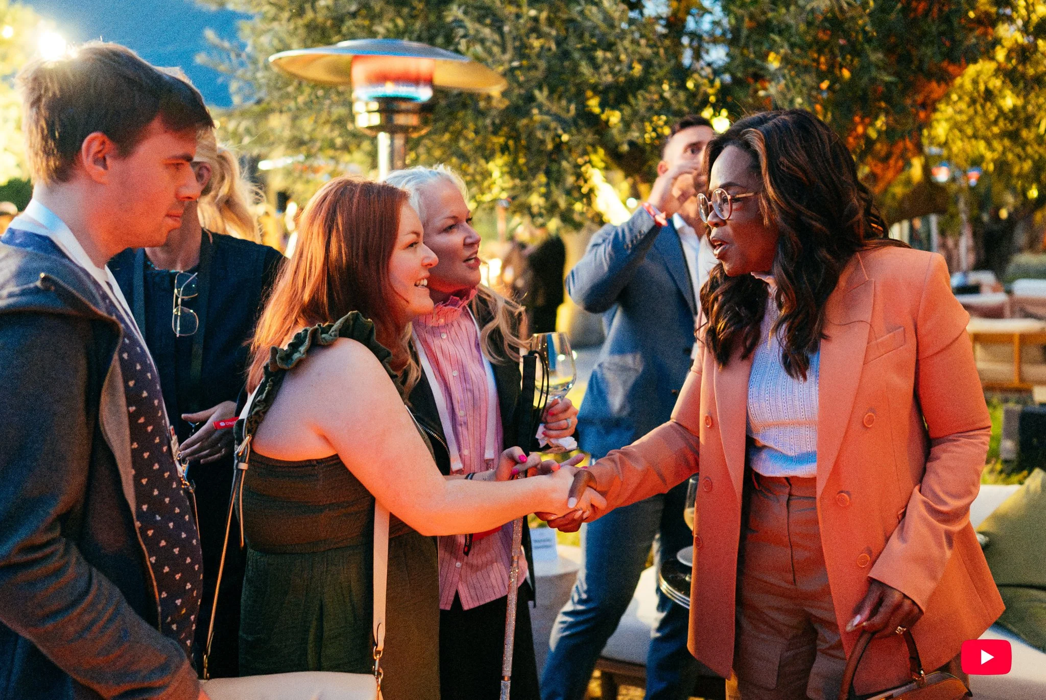 Lucy shakes hands and engages in conversation with Oprah who wears an orange blazer.
