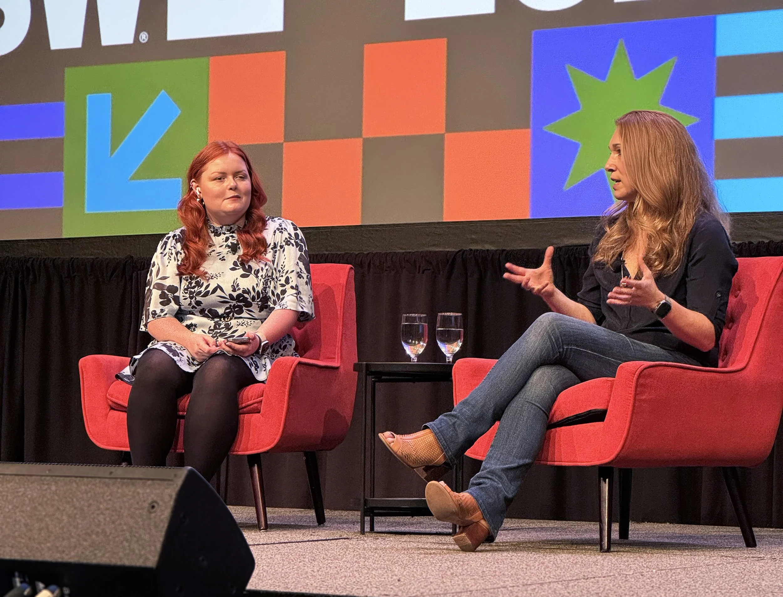 Lucy and head of accessibility at Apple Sarah Herrlinger sit on red chairs engaged in a discussion on stage at South by Southwest