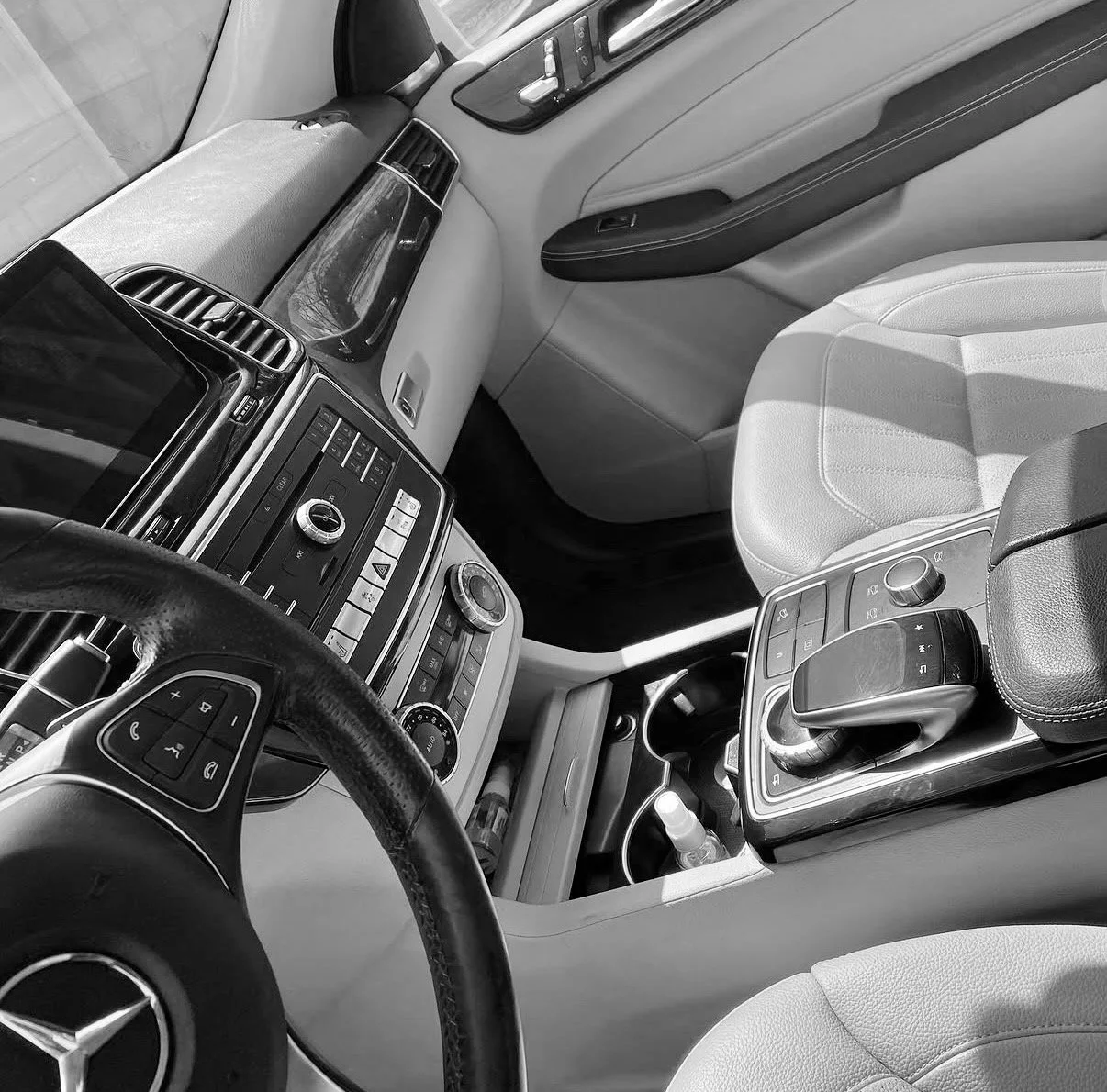 Interior of a Mercedes-Benz vehicle, showing the dashboard, steering wheel, and center console with gear shifter and controls in black and white.