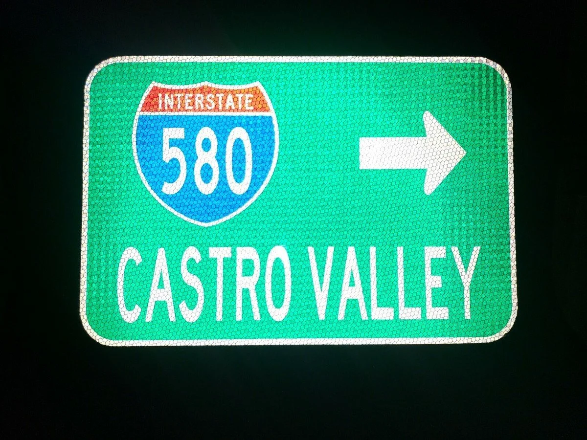 Reflective green road sign with white arrow pointing right, indicating directions to Interstate 580 and Castro Valley.