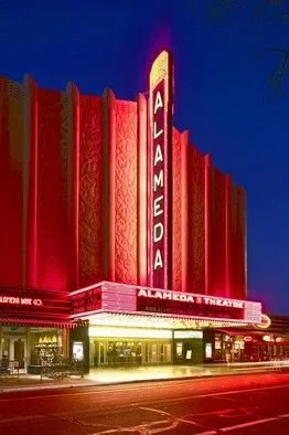 The Alameda Theatre with illuminated vertical ALAMEDA sign and bright marquee at night.