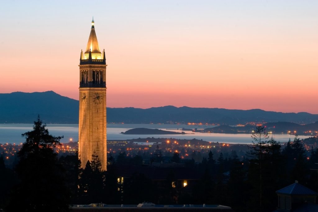 Sunset view of the historic Campanile tower in Berkeley, California, overlooking the city, bay, and surrounding mountains.