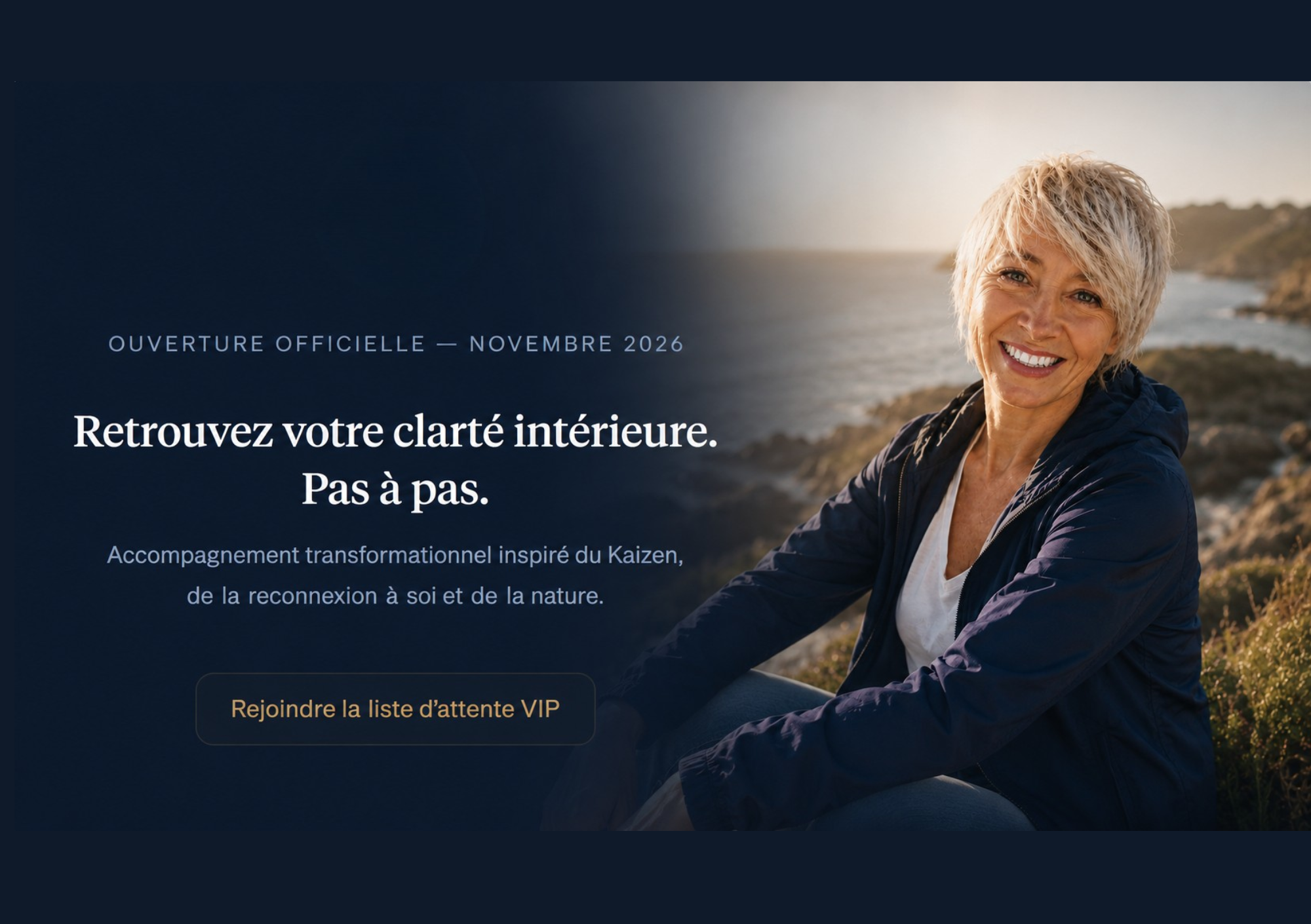 Une femme souriante avec des cheveux courts, blond cendré, portant une veste bleue marine, assise en extérieur près de la mer ou d’un littoral rocheux, par une journée ensoleillée.