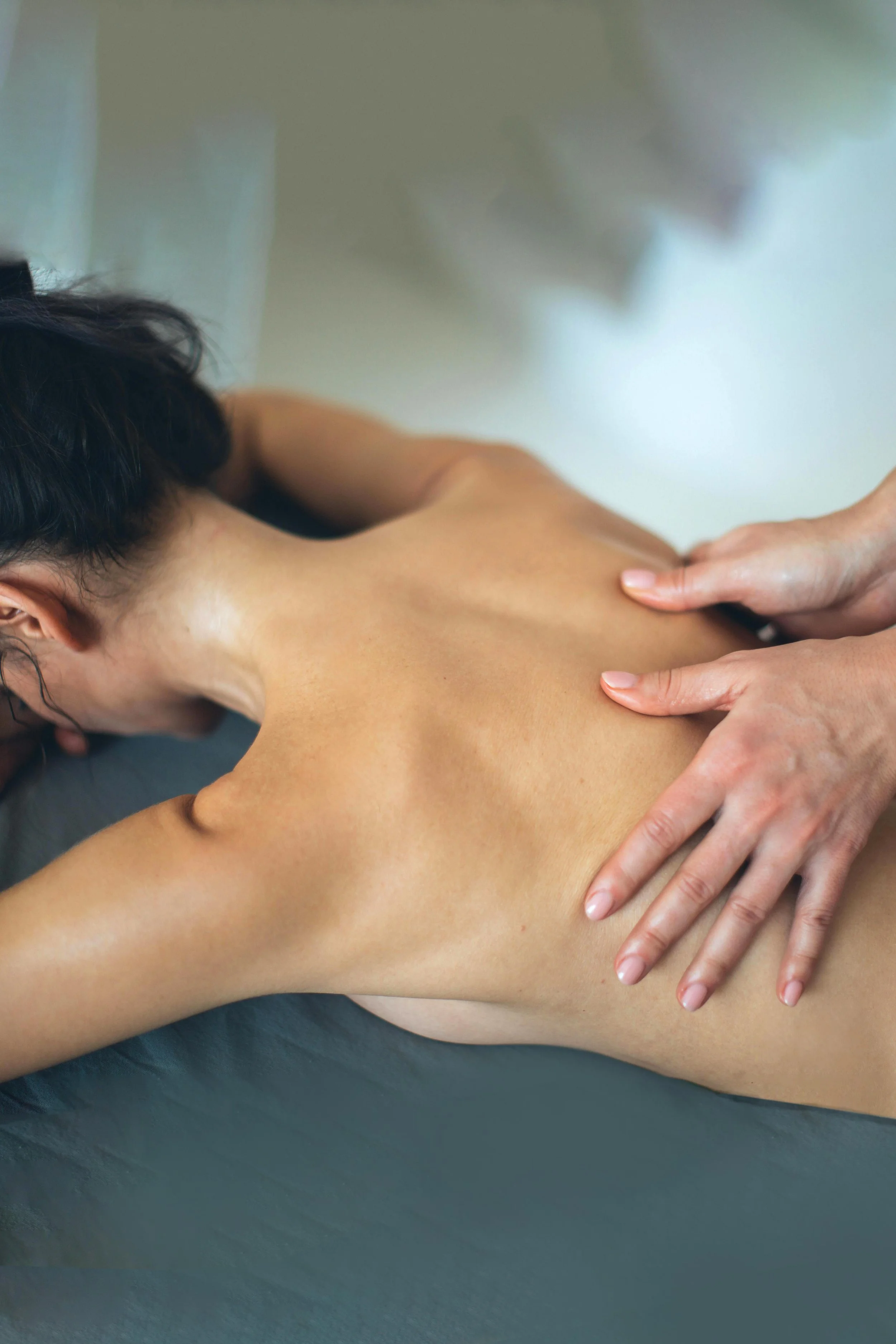 Une adolescente allongée recevant un massage sur le dos, avec une peau bronzée, dans un environnement calme.