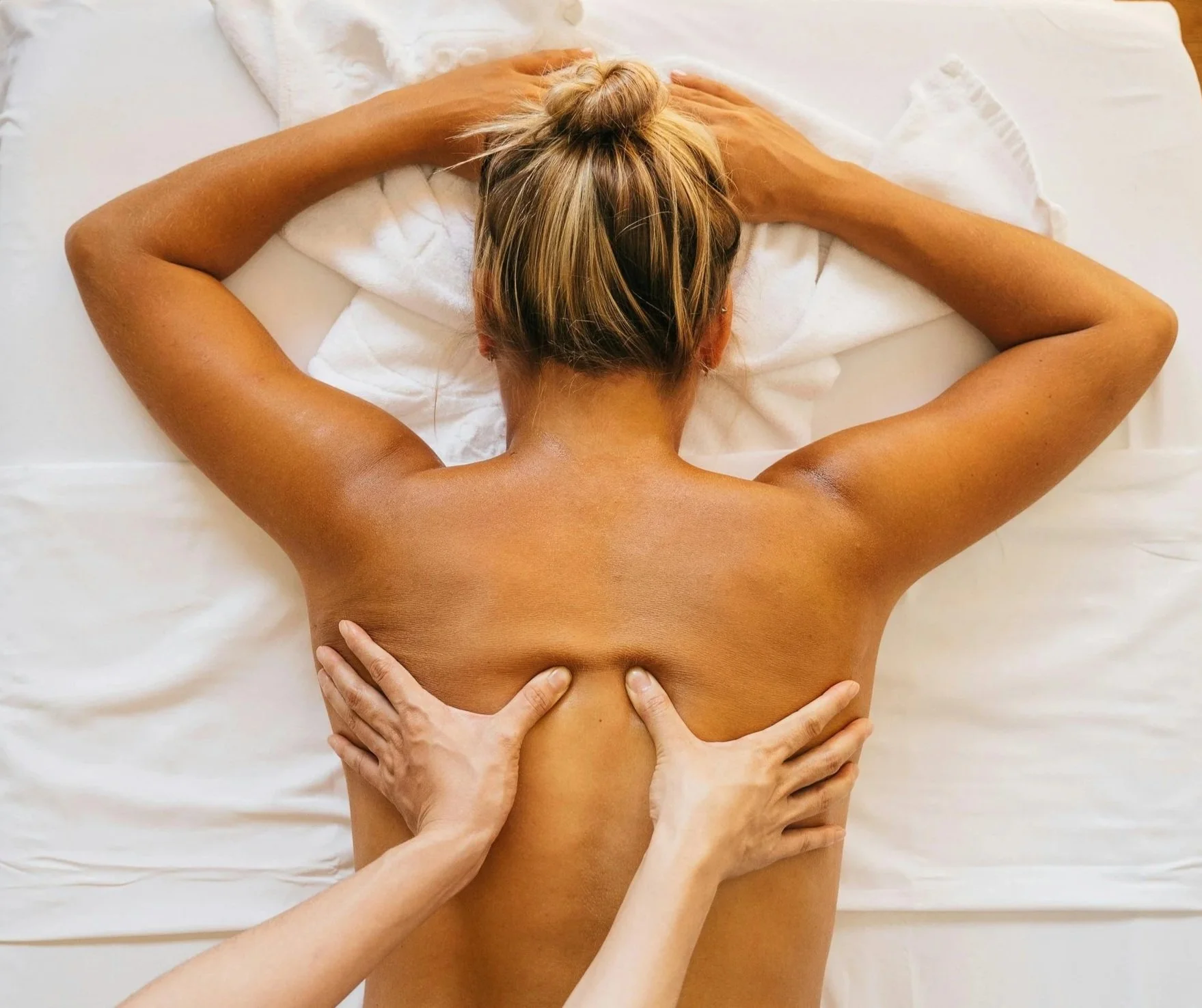 Une femme allongée sur le ventre recevant un massage de dos, vue de dessus, avec des mains qui la massent.