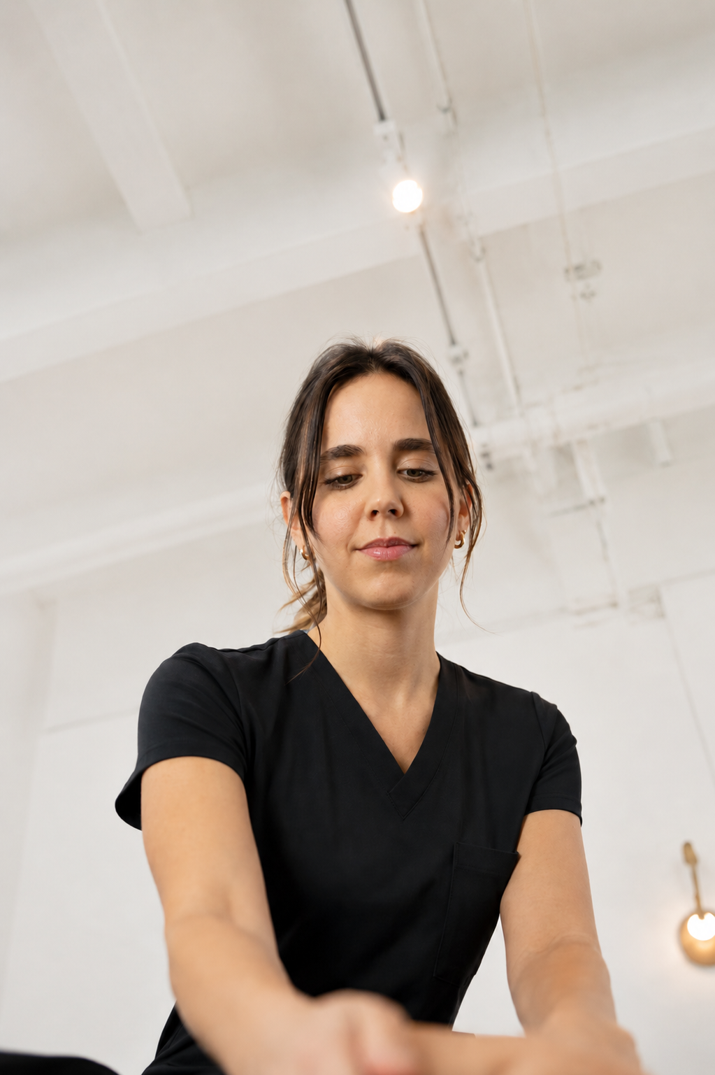 Une femme en uniforme noir se trouve dans un environnement intérieur avec un plafond en béton et des éclairages suspendus.