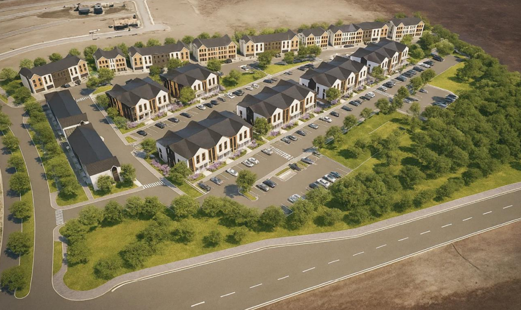 Aerial view of a modern residential apartment complex with multiple buildings, parking spaces, trees, and green spaces, surrounded by open land.