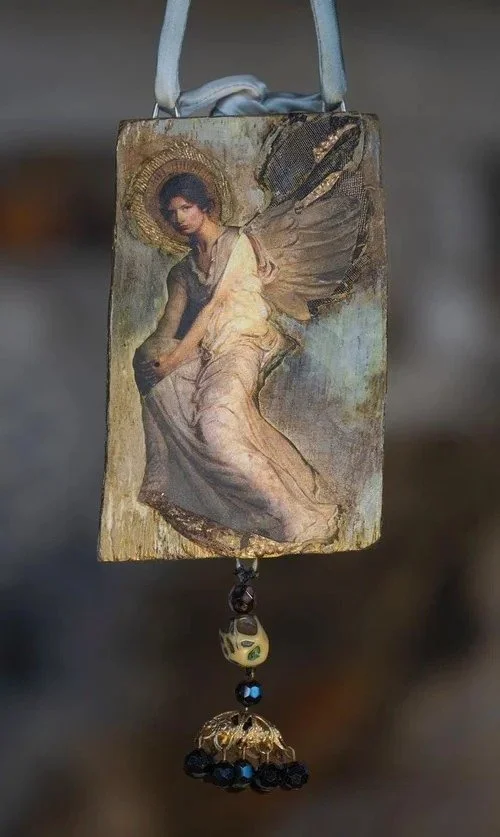 A handmade bag designed with a painted saint figure on the front, decorated with beads and charms hanging from the bottom.