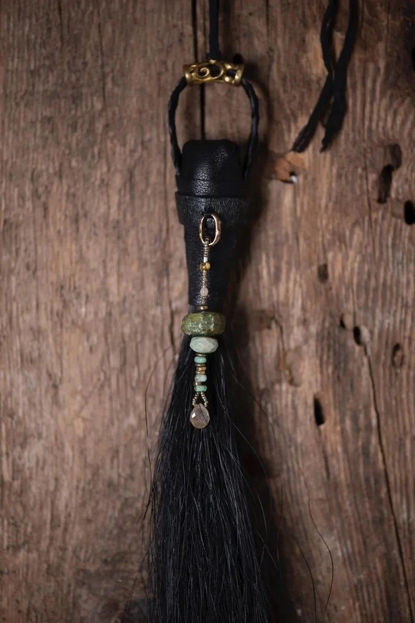 A decorative keychain with beads and a black tassel, hanging against a wooden background.