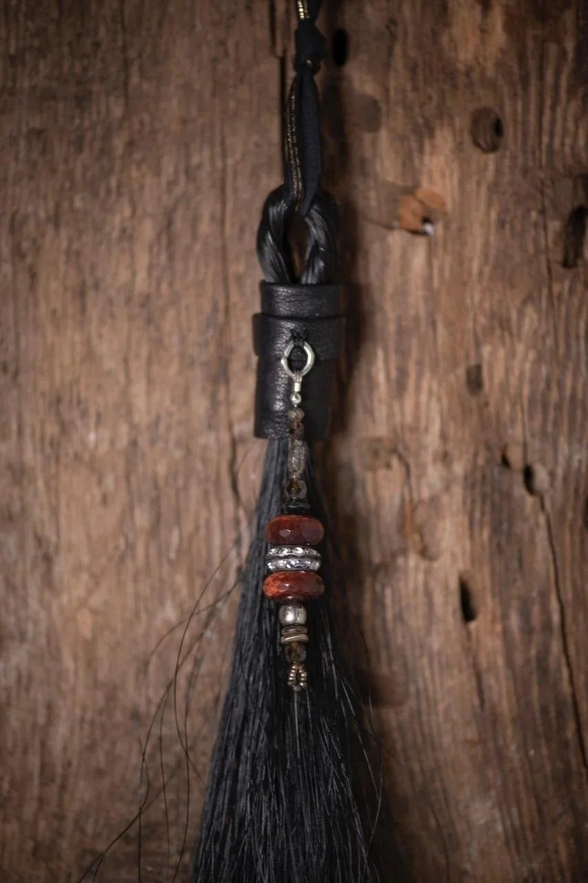 A hanging black leather and beaded whip or tassel against a wooden background.