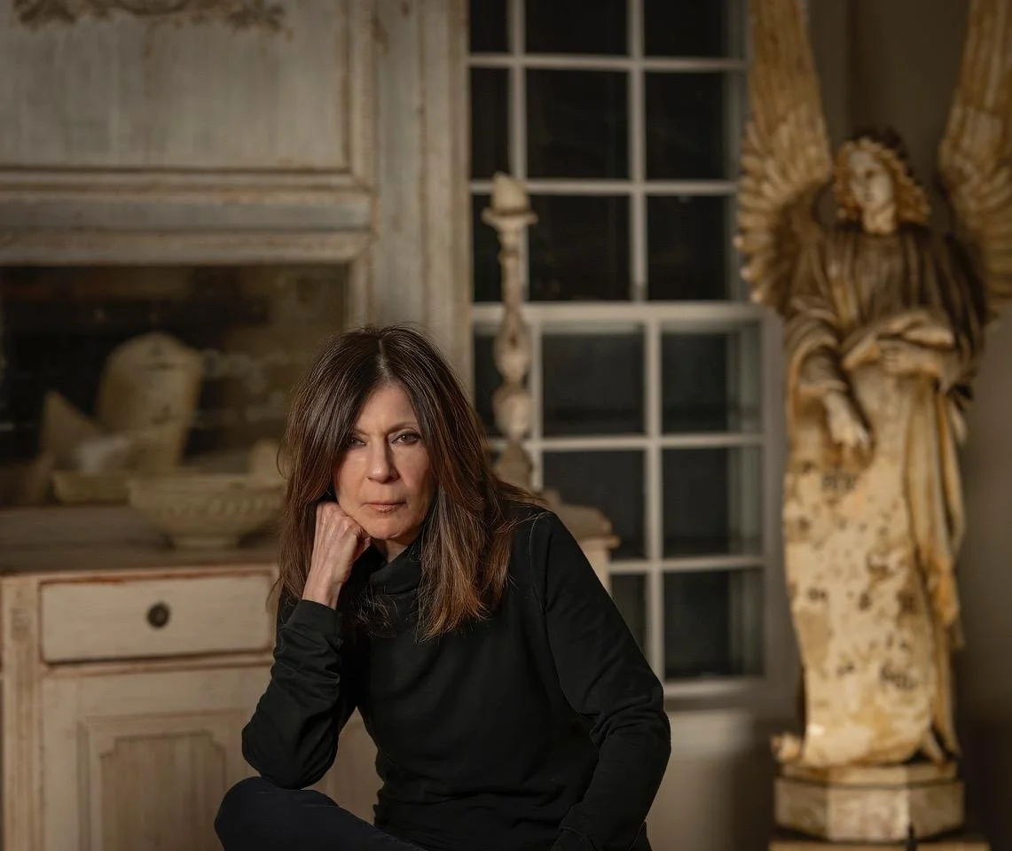 A woman in black clothing sitting in a room with artwork and sculptures in the background.