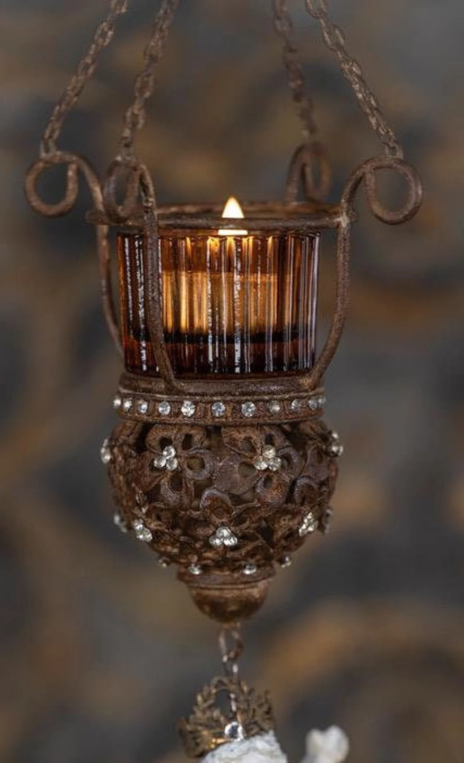 Close-up of an ornate hanging candle holder with a small lit candle inside, reflecting on a shiny surface.