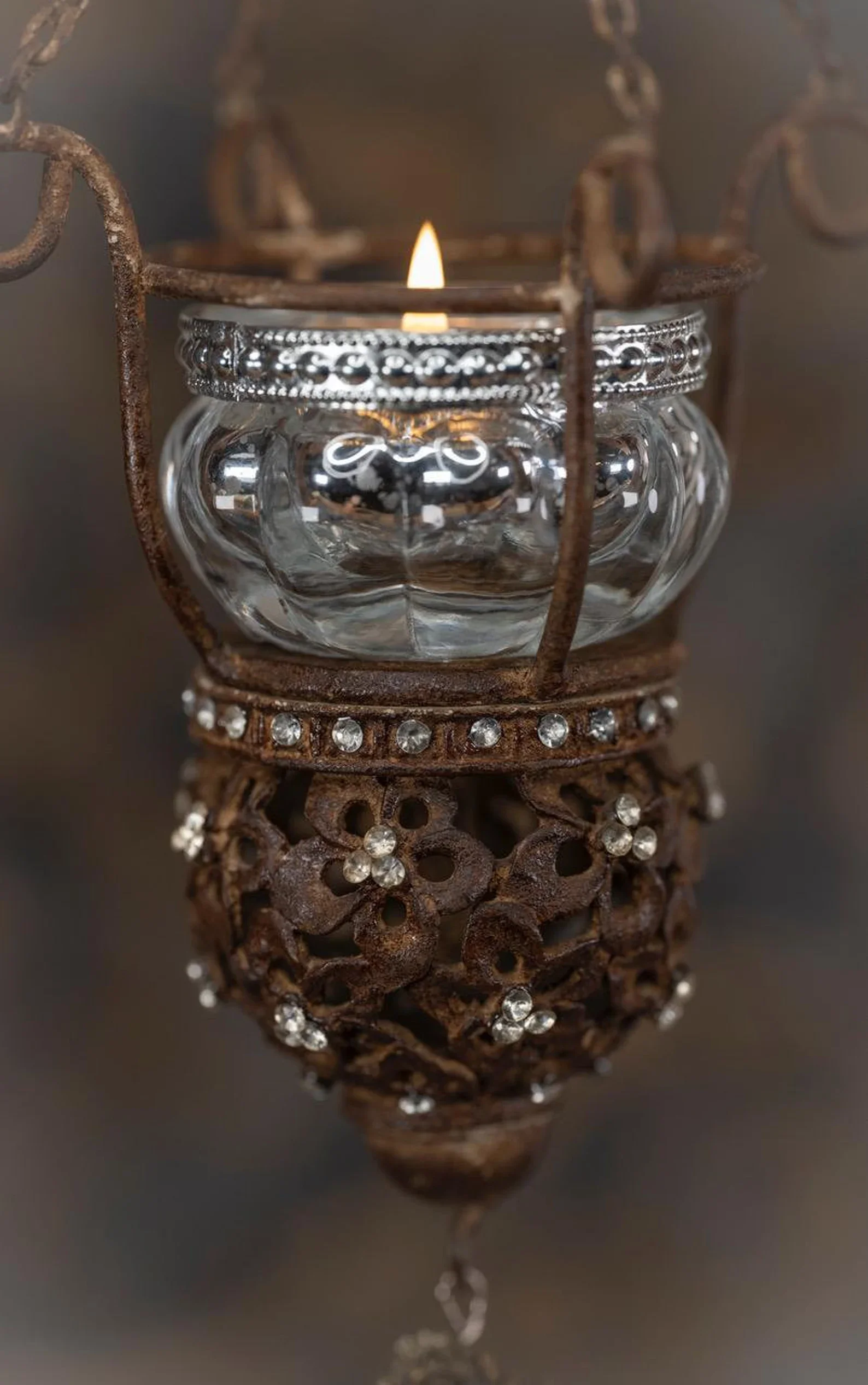 A small lit candle inside a glass holder surrounded by an ornate, rusted metal frame with decorative rhinestones.