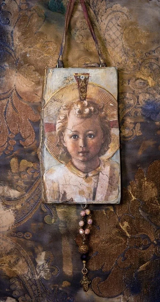 A vintage handbag with an artwork of a young girl with curly hair, a halo, and a solemn expression. The bag has a beaded strap and decorative elements hanging from the bottom.