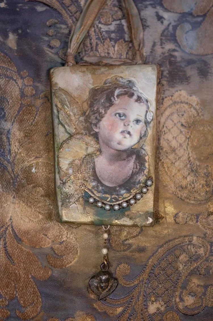 A vintage pendant necklace with a portrait of a young girl with curly hair, painted in a classical style, surrounded by gold-colored details, pearls, and a heart-shaped charm, all set against a textured fabric background.