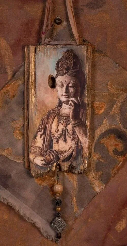 Wooden wall hanging with a painted image of a serene goddess or deity, holding a lotus flower, with intricate jewelry. There is a hole in the wood, and a string of beads and a decorative pendant hanging from the bottom.