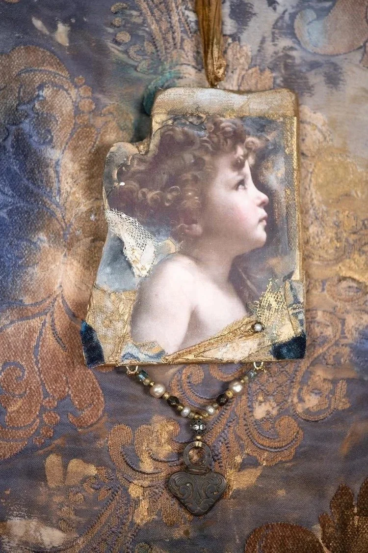 An antique picture frame containing a portrait of a young child with curly hair, placed on ornate patterned fabric. A beaded necklace with a large decorative pendant is draped below the frame.