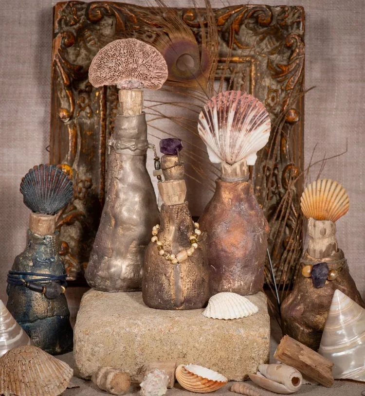 Decorative arrangement of natural objects including shells, peacock feathers, stones with metallic finishes, and jewelry, displayed against a carved wooden frame.