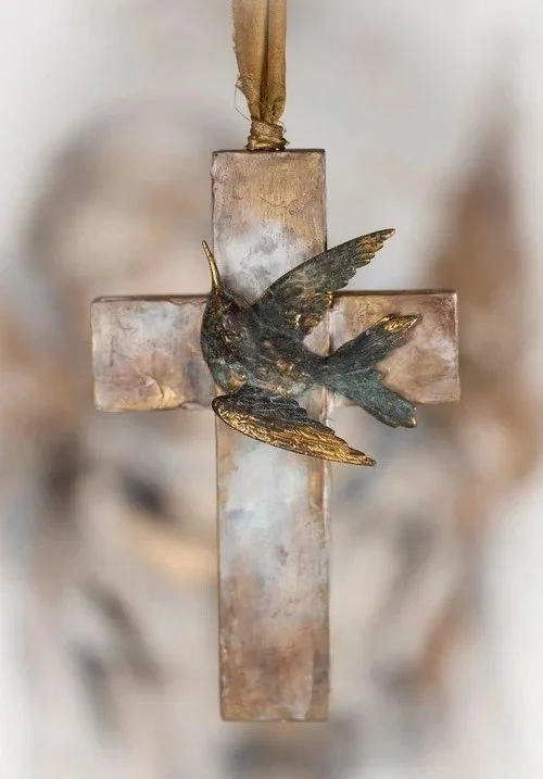 Metal cross with a small metal bird attached, hanging by a ribbon.