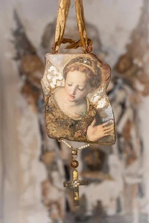 A hanging religious pendant with a vintage image of a woman holding a rosary and a crucifix, against a blurred background.