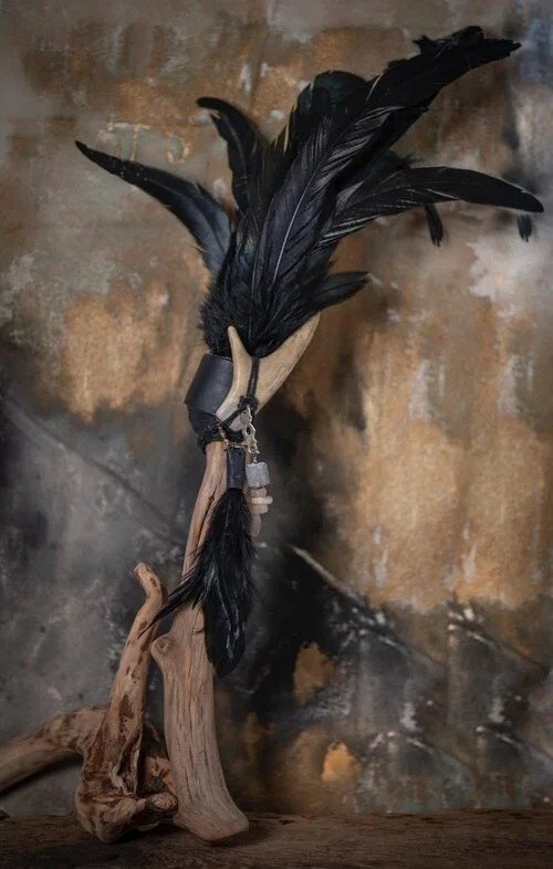 Decorative item made of a piece of driftwood with black feathers attached, resembling a small sculpture or bird