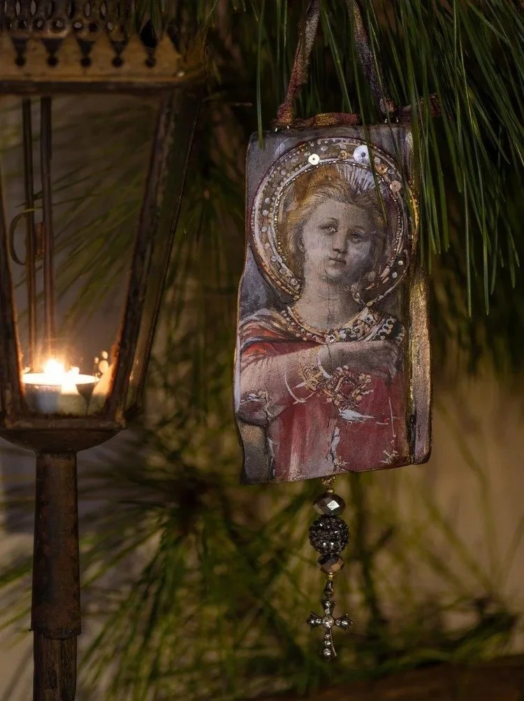 Hanging religious icon depicts a woman with a halo, dressed in red, next to a lit candle in a lantern.
