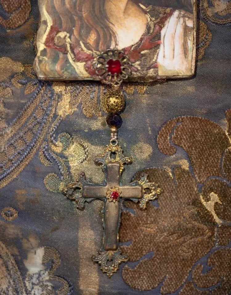 A vintage rosary with a silver cross and red gemstones, laid on ornate fabric with a religious-themed picture of Jesus.