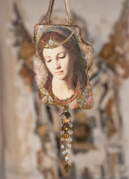 A decorative religious pendant featuring a portrait of the Virgin Mary, with beads and a small cross hanging from it.