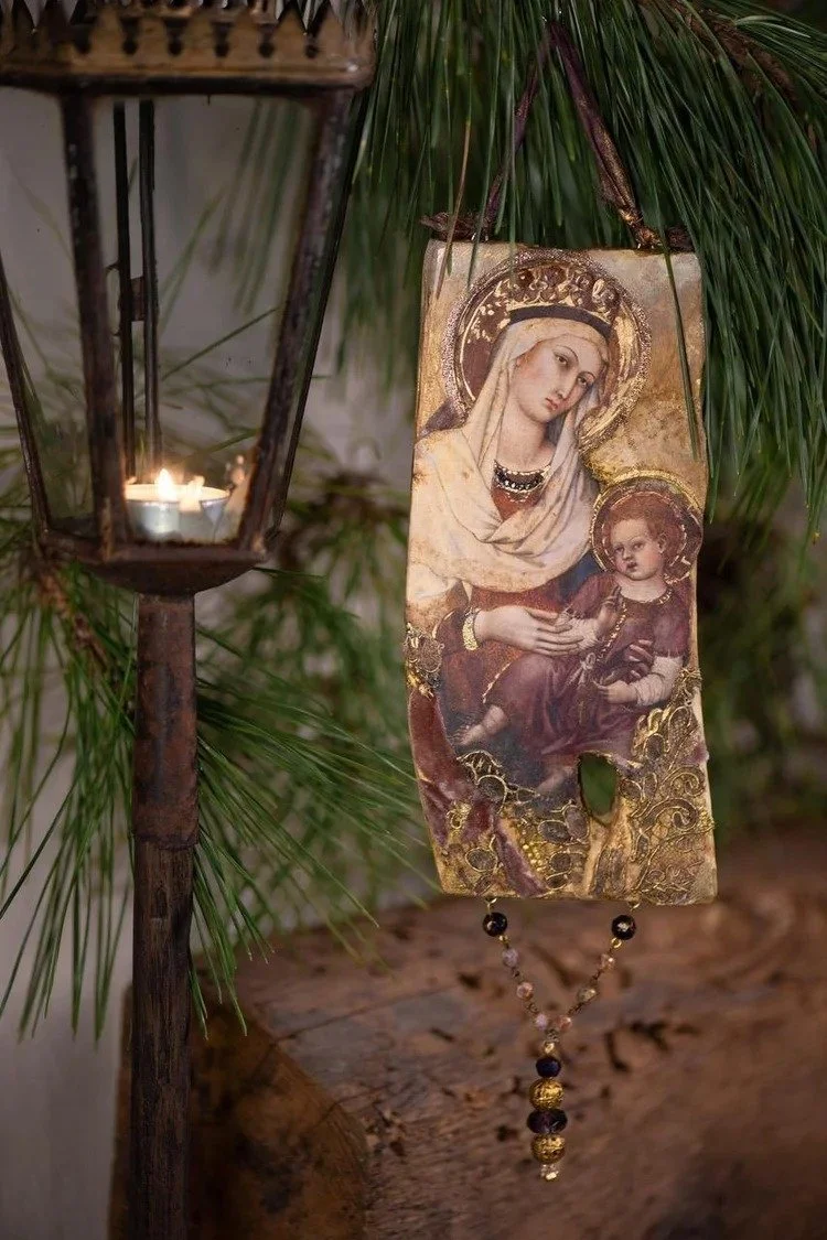 A religious icon depicting the Virgin Mary and baby Jesus, hanging from a branch, with a candle lantern nearby.