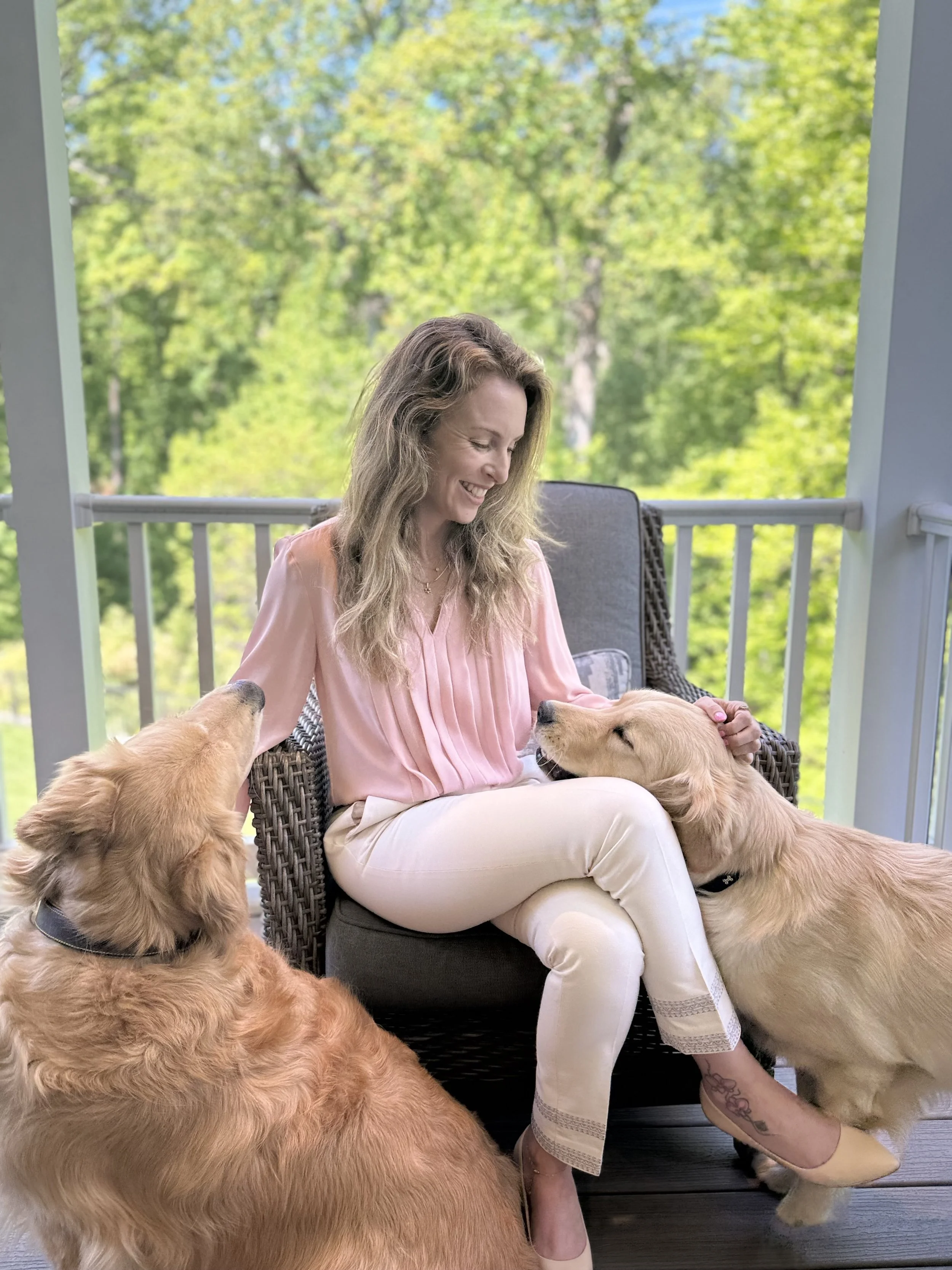 Hilla Flohr sitting on a porch with her golden retrievers, sharing a calm and connected moment
