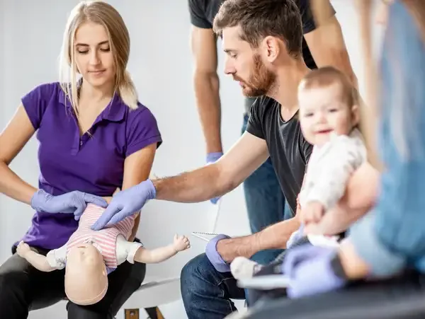 Medical professionals practicing Pediatric Advanced Life Support on a baby mannequin in a hospital or training setting.