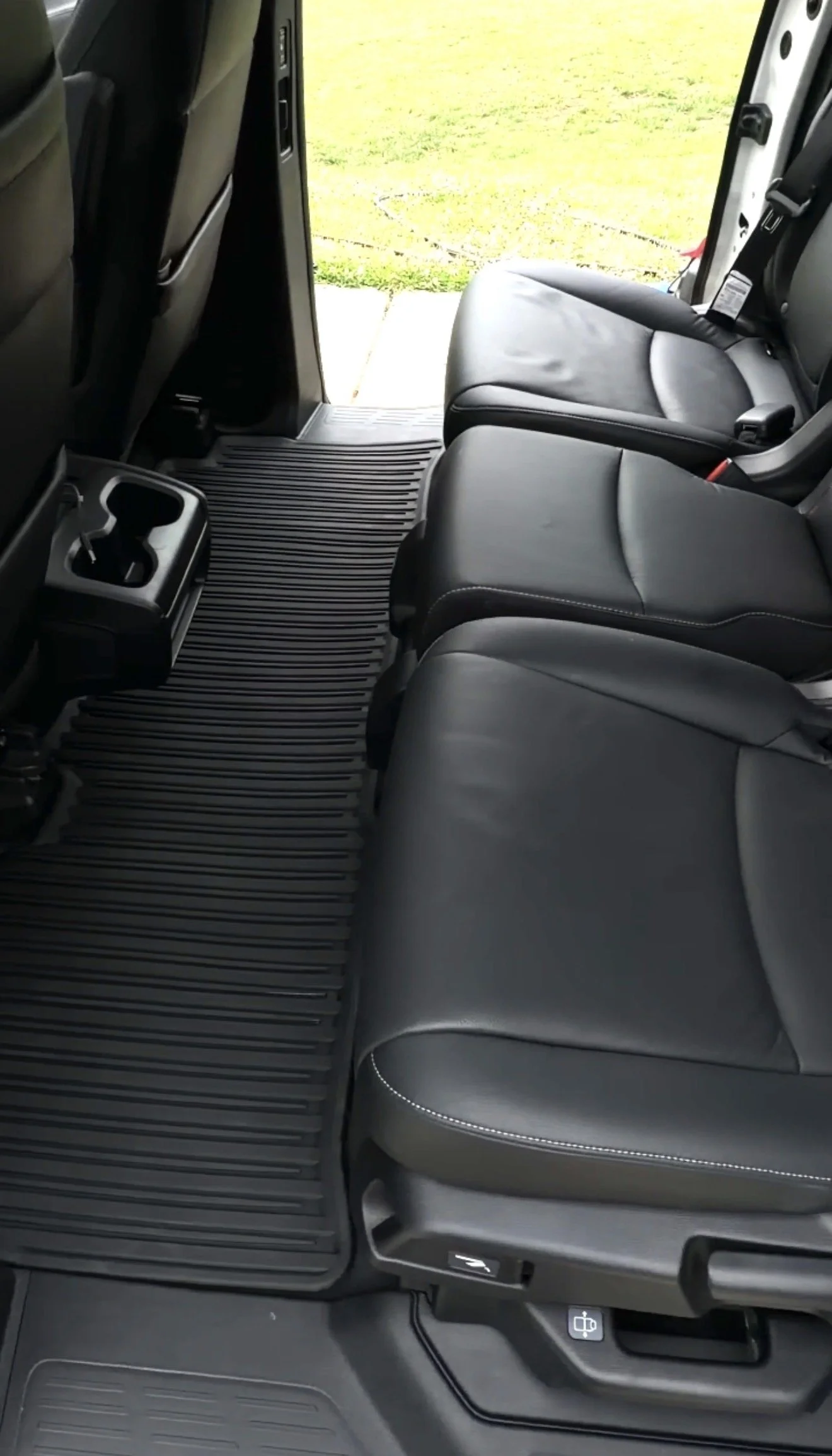 Interior of a vehicle showing the back seats, floor mats, and the open door with a view of grass outside